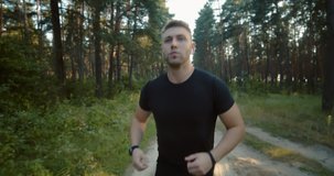 Front view of active young man in black t-shirt running among green forest during summer time. Fitness, healthy, lifestyle concept.