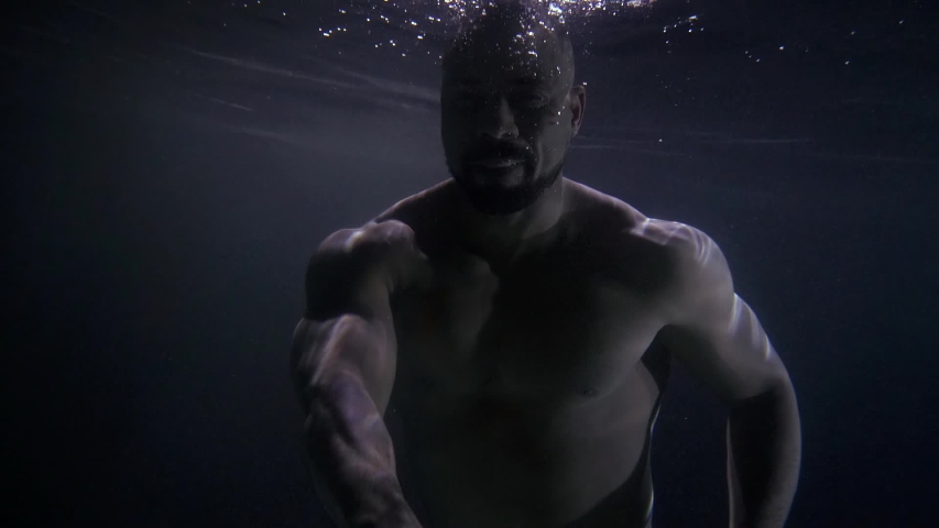 Black man is swimming underwater, sinking in depth, moving hands, medium portrait | Shutterstock HD Video #1057458739