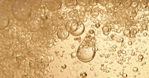 Fuel, oil, yellow golden hue, with moving bubbles, up and down, in the glass vessel of the laboratory. Copy space. Macro oil and water interacting