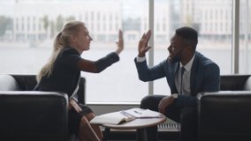 Side view of two multiethnic business colleagues sharing high five sitting on couch in office hall. Man and woman in formal wear chatting sitting on sofa and giving high five during break at work - Powered by Shutterstock - Get 15% off with code: PIKWIZARD15