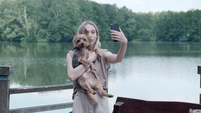 A beautiful young girl is resting on the lake with a dog and takes a selfie.