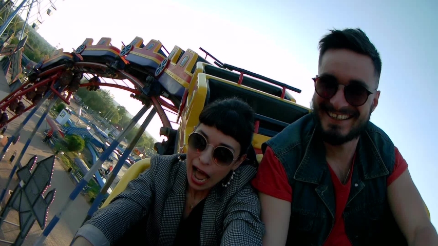 Selfie video of couple riding the roller coaster. Hipster man and stylish woman have fun at amusement park rides. Friends extreme riding, laughing and screaming of excitement, adrenalin. Royalty-Free Stock Footage #1057479814