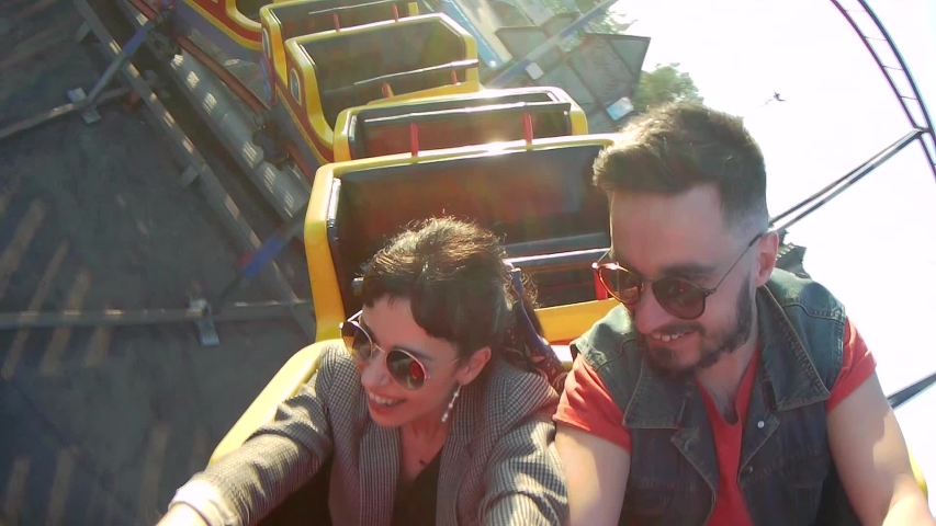 Selfie video of couple riding the roller coaster. Hipster man and stylish woman have fun at amusement park rides. Friends extreme riding, laughing and screaming of excitement, adrenalin. | Shutterstock HD Video #1057479814