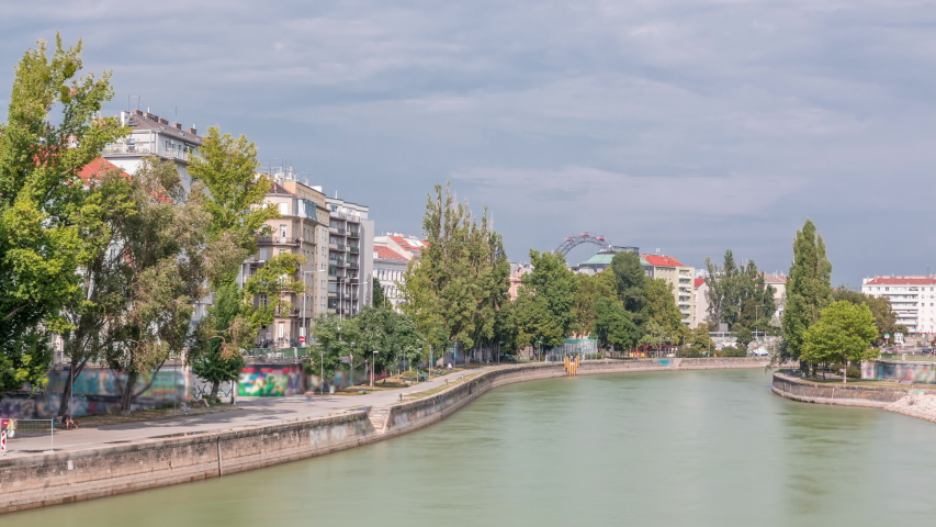 Vienna cityscape with the Danube channel timelapse in Vienna. Austria. Buildings with green trees and ferris wheel on a background