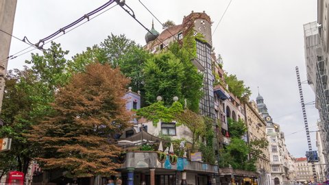 The Hundertwasserhaus apartment block timelapse hyperlapse has colorful facade, undulating floors, a roof covered with earth and grass, and large trees growing from inside the rooms. Vienna, Austria