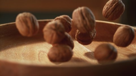 In a beautiful light, walnuts fall into the wooden plate in slow motion. 4K,Very close up, phantom camera,900 fps video.