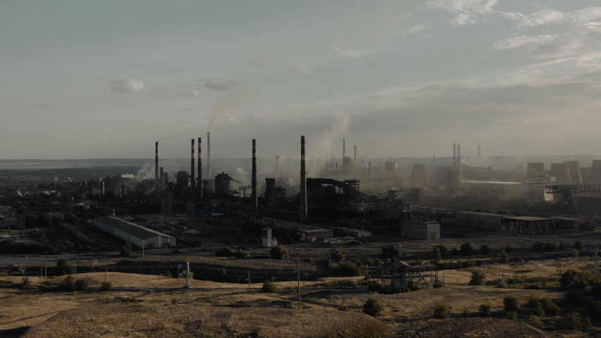 Drone shot of grey industrial city area with thick smog and burning fossil fuels. Factory zone zoom in of factory, chimneys in city area near green field | Shutterstock HD Video #1057488784