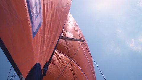 Orange mainsail and staysail of a sailboat lower anlge view on the sky background. Travel and summer concept.