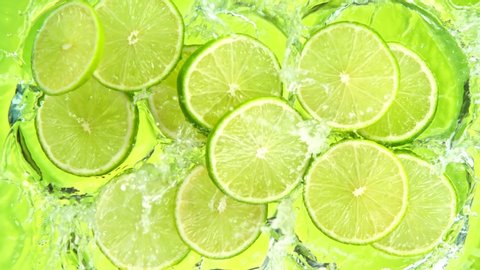 Super Slow Motion Shot of Lime Slices Falling into Water on Green Background at 1000fps.