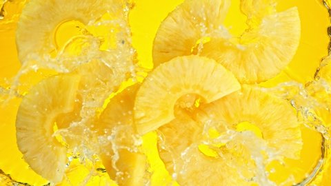 Super Slow Motion Shot of Pineapple Slices Falling into Water on Yellow Background at 1000fps.
