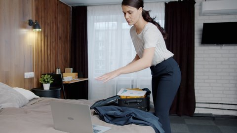 Young businesswoman is packing bag putting things in suitcase in hotel room finishing business trip. People, lifestyle and accommodation concept.