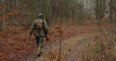 Historical Re-enactment. Re-enactor Dressed As American Soldier Of USA Infantry Of World War II Marching Walking Along Forest Road In Autumn Day. Soldier Marching In Forest.