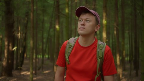 Young man in a cap walks through the forest looks around, tracking with a camera
