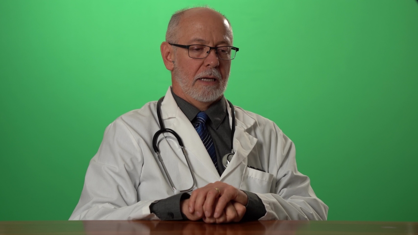 Male doctor wearing a lab coat and stethoscope on green screen sitting at desk dealing with depression or grief. Royalty-Free Stock Footage #1057497142