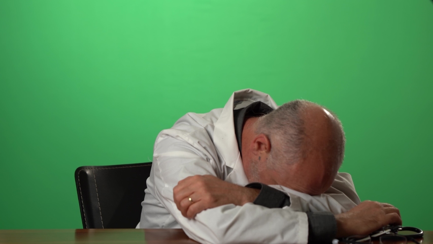 Male doctor wearing a lab coat and stethoscope on green screen sitting at desk dealing with depression or grief. Royalty-Free Stock Footage #1057497172