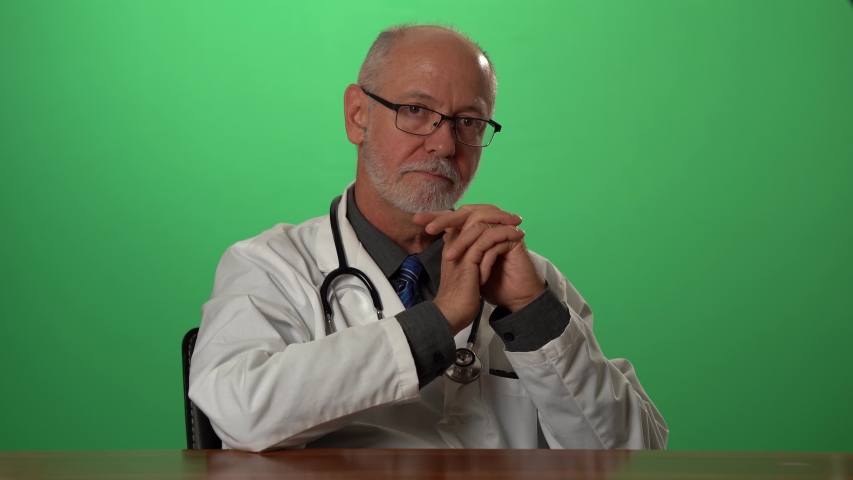 Male doctor wearing a lab coat and stethoscope on green screen sitting at desk dealing with depression or grief. Royalty-Free Stock Footage #1057497187