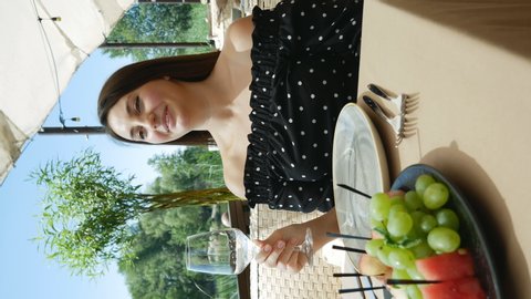 a young woman, a girl sits at a table in a restaurant and blinks her eyes coquettishly. Creation of fun youthful content on social media. vertical video
