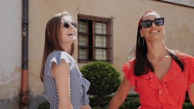 Portrait view of two best cheerful tourists in a stylish look in sunglasses and summer dresses playfully dance and having fun in urban street,posing to camera. Blonde and brunette