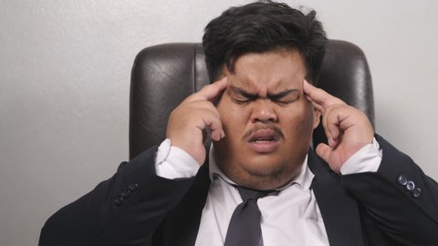 A funny Asian fat businessman wearing a suit look like the head of corporate executive or business manager is thinking so hard that he has a headache and a debilitating health. 