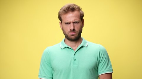 upset casual man grimacing, frowning and making an angry face, standing on yellow background
