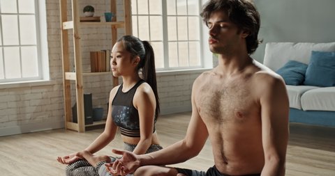 Multiethnic couple doing yoga at home. Young fit family sitting on the floor, meditating together, keeping a healthy lifestyle during lockdown - fitness concept 4k footage