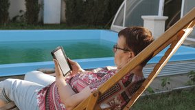An elderly retired woman sitting by the pool in the backyard of the house with interest reading an e-book. - Powered by Shutterstock - Get 15% off with code: PIKWIZARD15