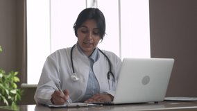 Indian telemedicine doctor wear headset consulting patient by online video call on laptop. Female gp talking with client in remote telehealth conference video chat in India. Virtual meeting visit.