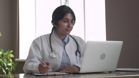 Indian telemedicine doctor wear headset consulting patient by online video call on laptop. Female gp talking with client in remote telehealth conference video chat in India. Virtual meeting visit.