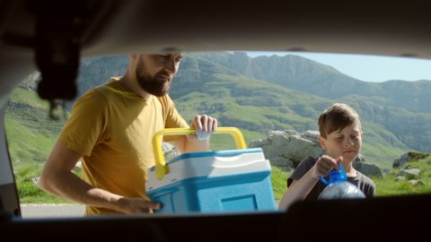 Happy father and son putting in car trunk things and bags against mountain landscape in Montenegro. Family vacation 
