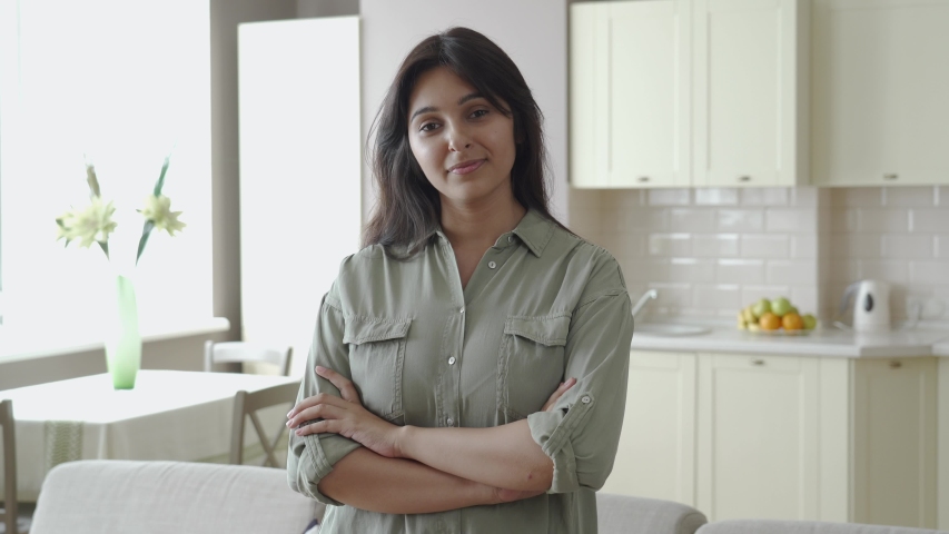 Smiling confident young pretty indian ethnic woman looking at camera standing alone at home in apartment kitchen arms crossed. Happy beautiful single millennial lady in India indoor, headshot portrait Royalty-Free Stock Footage #1057533316
