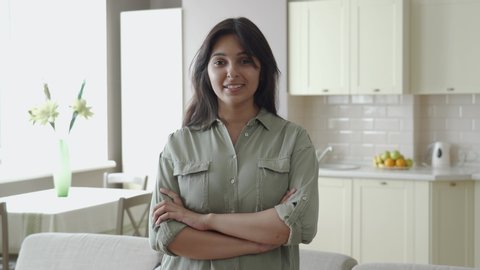 Smiling confident young pretty indian ethnic woman looking at camera standing alone at home in apartment kitchen arms crossed. Happy beautiful single millennial lady in India indoor, headshot portrait