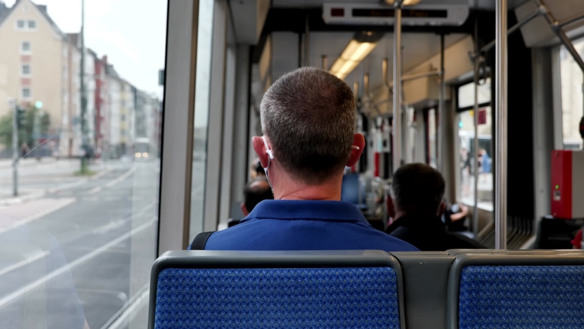 Interior and selected focus view at the back of male passenger with face protection mask who sit in light rail tram or train in Germany during epidemic of COVID-19 virus with new normal concept. Royalty-Free Stock Footage #1057535758