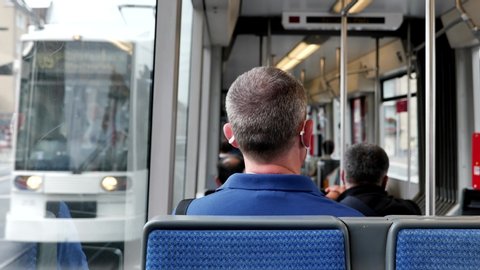 Interior and selected focus view at the back of male passenger with face protection mask who sit in light rail tram or train in Germany during epidemic of COVID-19 virus with new normal concept.