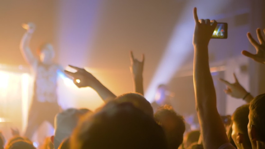 Super slow motion: people crowd partying, raising hands up, showing sign - devil's horns gesture and jumping at rock concert in front of stage of nightclub. Nightlife and entertainment concept | Shutterstock HD Video #1057536691