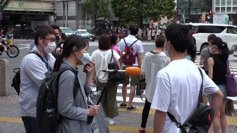SHIBUYA, TOKYO, JAPAN - AUG 2020 : Crowd of people wearing surgical mask to protect from Coronavirus (COVID-19) at Shibuya Crossing. Young man being interviewed by TV crew (News reporter).