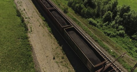 Freight long train carries with coal carriages an electric locomotive by two-sided Trans Siberian railways under the rock and near mountains river / Aerial drone wide view at summer sunny day
