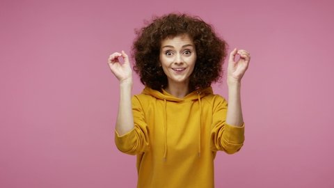 Curious  young woman afro hairstyle in hoodie looking through hands binocular gesture, zooming observing distance, expressing surprise shock happiness after seen discovery. indoor studio shot isolated