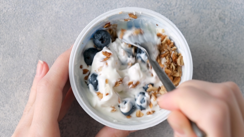 Yogurt with granola and blueberries in a jar. Female eating healthy breakfast fitness yoga food, sustainable eating | Shutterstock HD Video #1057556542