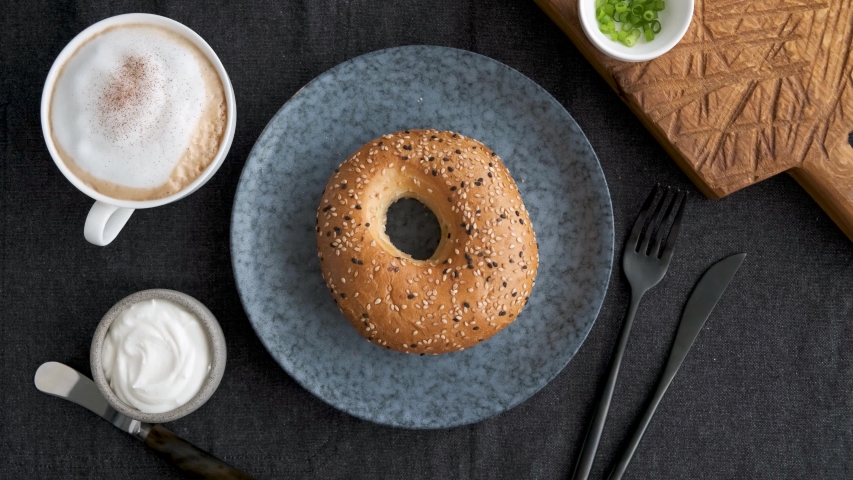 Spreading cream cheese on bagel. Female chef prepare toasted bread sandwich with cream cheese for breakfast, top view