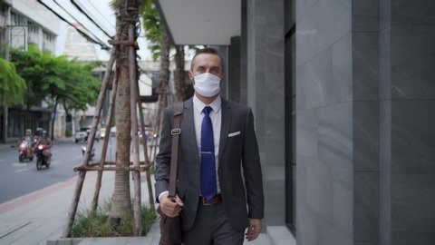 Handsome Caucasian business man office worker in suit walking in city street to office district for working. Business man wearing face mask during protect covid-19 virus pandemic. New normal concept.: film stockowy