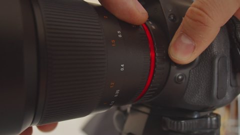 The lens is detached from the camera mount. A man's hand presses the lens mount button and detaches the lens from the camera. Close-up of disconnecting lens from the camera