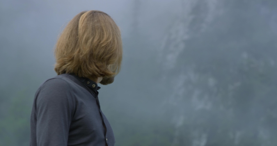 Close up Shot, Man in black shirt Turning his shoulder and head around, blurred mountain in the background.