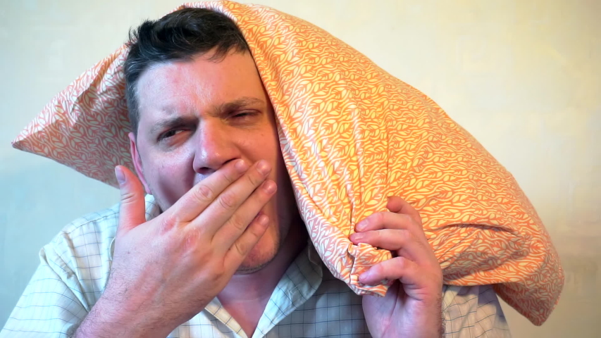 portrait of a bored yawning man who covers his head with a pillow.