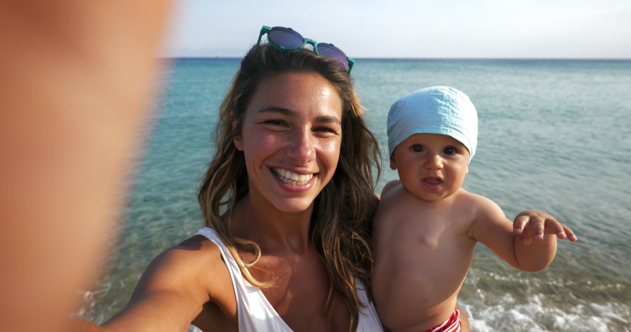 A happy carefree smiling neo mother and her newborn baby making selfie or video call to father or relatives on a beach with seaside in a sunny day. Royalty-Free Stock Footage #1057566577