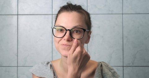 Portrait of woman in glasses pretending shaving her beard in bathroom, front view. She is looking at camera and smiling. Joke, funny video in slow motion.