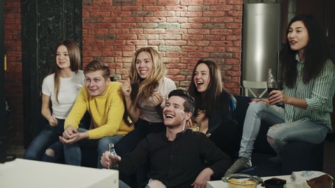 Millenials in living room happy and celebrating victory by hugging and screaming. Group of teenagers watching sport event on television with excitement and cheering. Concept of leisure, lifestyle, tv.