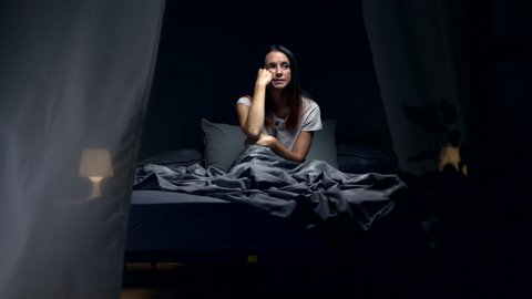 Sad woman suffering from insomnia and heat, she is sitting in bed and thinking