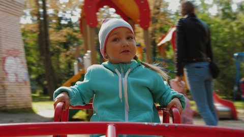 Portrait of cute little girl having fun on merry-go-round, she smiles and happy. A handsome emotional kid rides on carousel at children playground in park, real emotions.