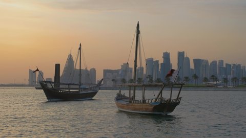 Doha skyline from the corniche promenade sunset shot showing dhows with Qatar flag in the Arabic gulf  in foreground and clouds in the sky in background