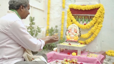 Senior man worshiping lord ganesh by offering aarti during vinayaka Chaturthi festival pooja or ritual  celebration at home in India.